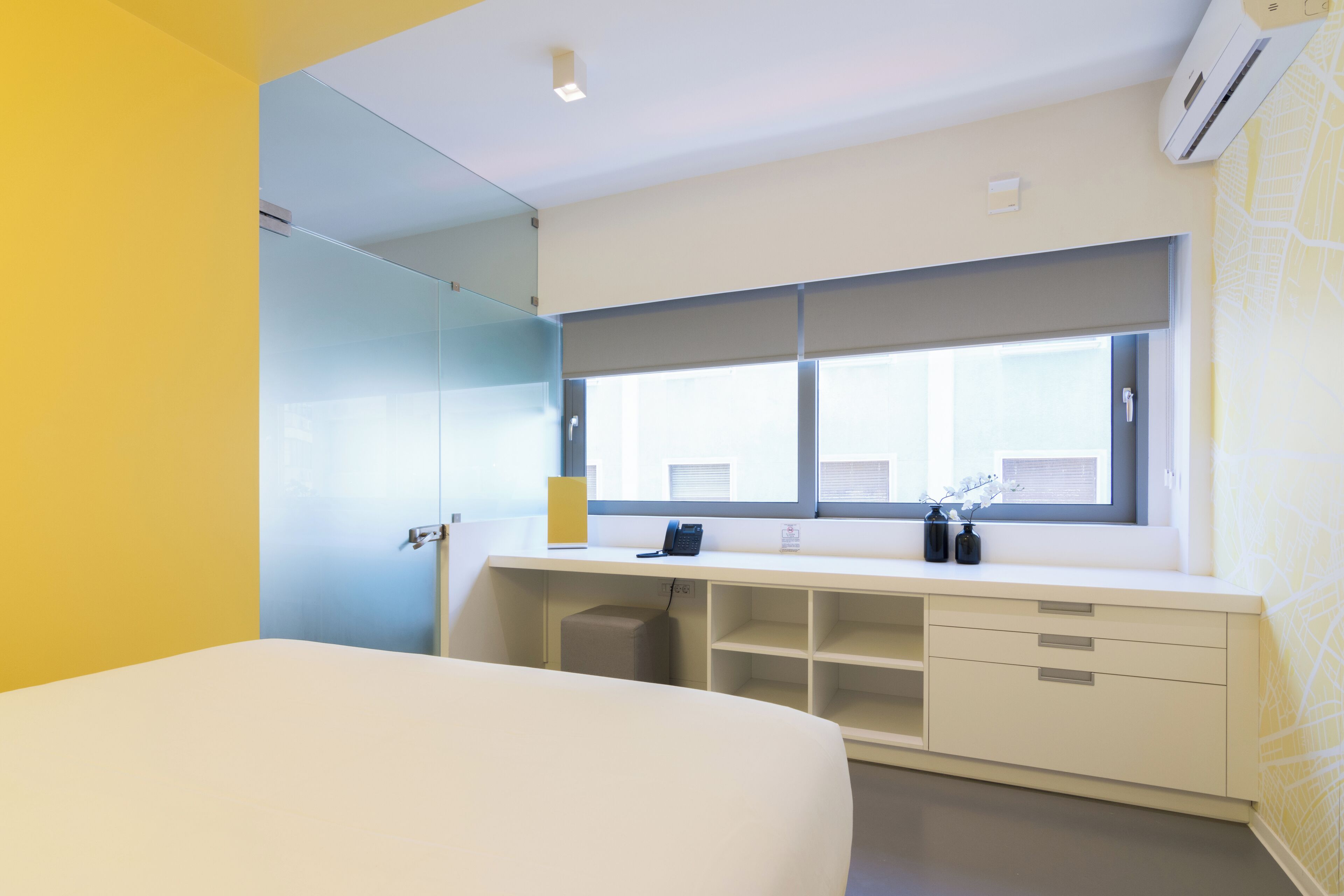 Une chambre d’hôtel moderne avec un grand lit, un bureau équipé d’un ordinateur et une fenêtre avec des stores.