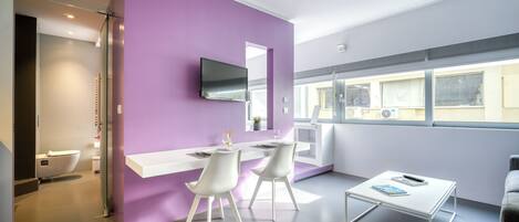 Una cucina moderna con una parete viola a contrasto, mobili bianchi e una TV a schermo piatto montata sopra il bancone.