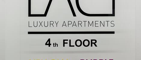 A sign for Athens Colorcube Luxury Apartments on the 4th floor, indicating available colors: Yellow, Purple, Aqua, Blue, and Green.