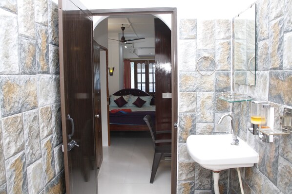 A narrow hallway leading to a bedroom with a bed, a bathroom with a sink and mirror, and stone-patterned walls.