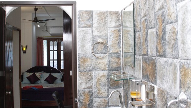 A bathroom with a stone wall sink, a mirror, and a showerhead. - Ratnoop Inn-enjoy the classic stay (Port Blair)