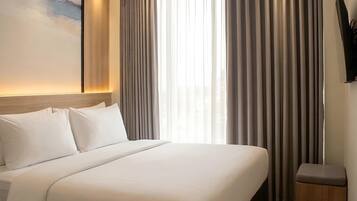 A hotel room with a bed, curtains, a wall-mounted TV, and a painting.