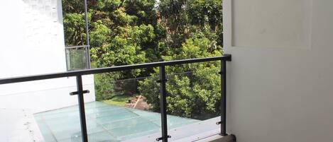 Uma varanda com piso de vidro, guarda-corpo de metal e vista para um jardim exuberante.