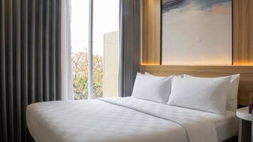 A hotel room with a large bed, a view of trees outside, and a modern abstract painting on the wall.