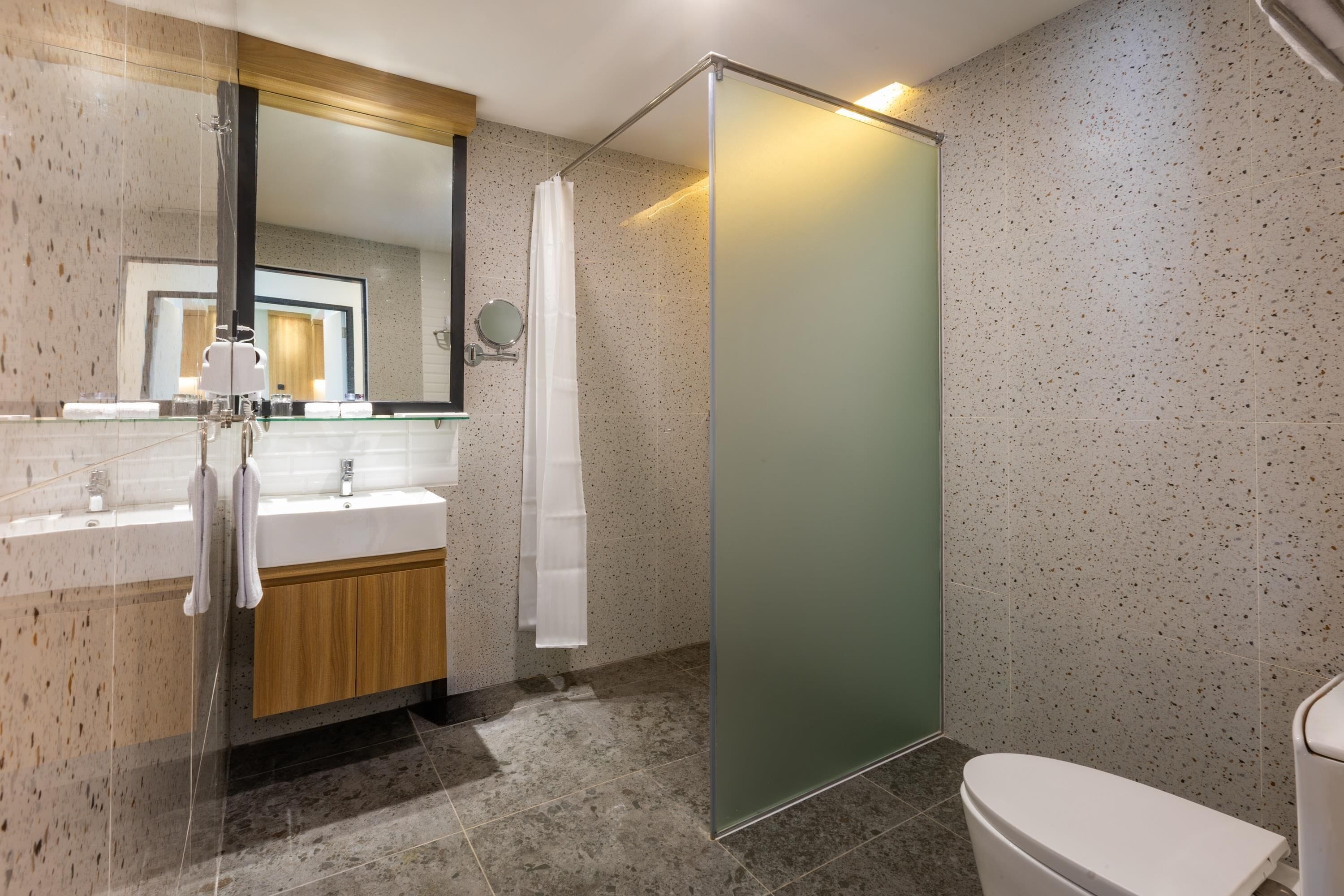 Un baño moderno con cabina de ducha de vidrio, tocador de madera, inodoro blanco y un espejo grande.