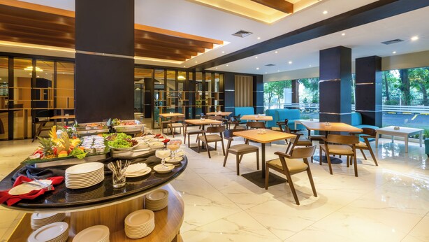 A modern dining area with a buffet setup, multiple seating arrangements, and large windows offering a view of the outdoors. - Best Western Setiabudhi Bandung (Bandung)