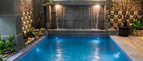 A swimming pool with a waterfall feature, surrounded by stone walls and potted plants.