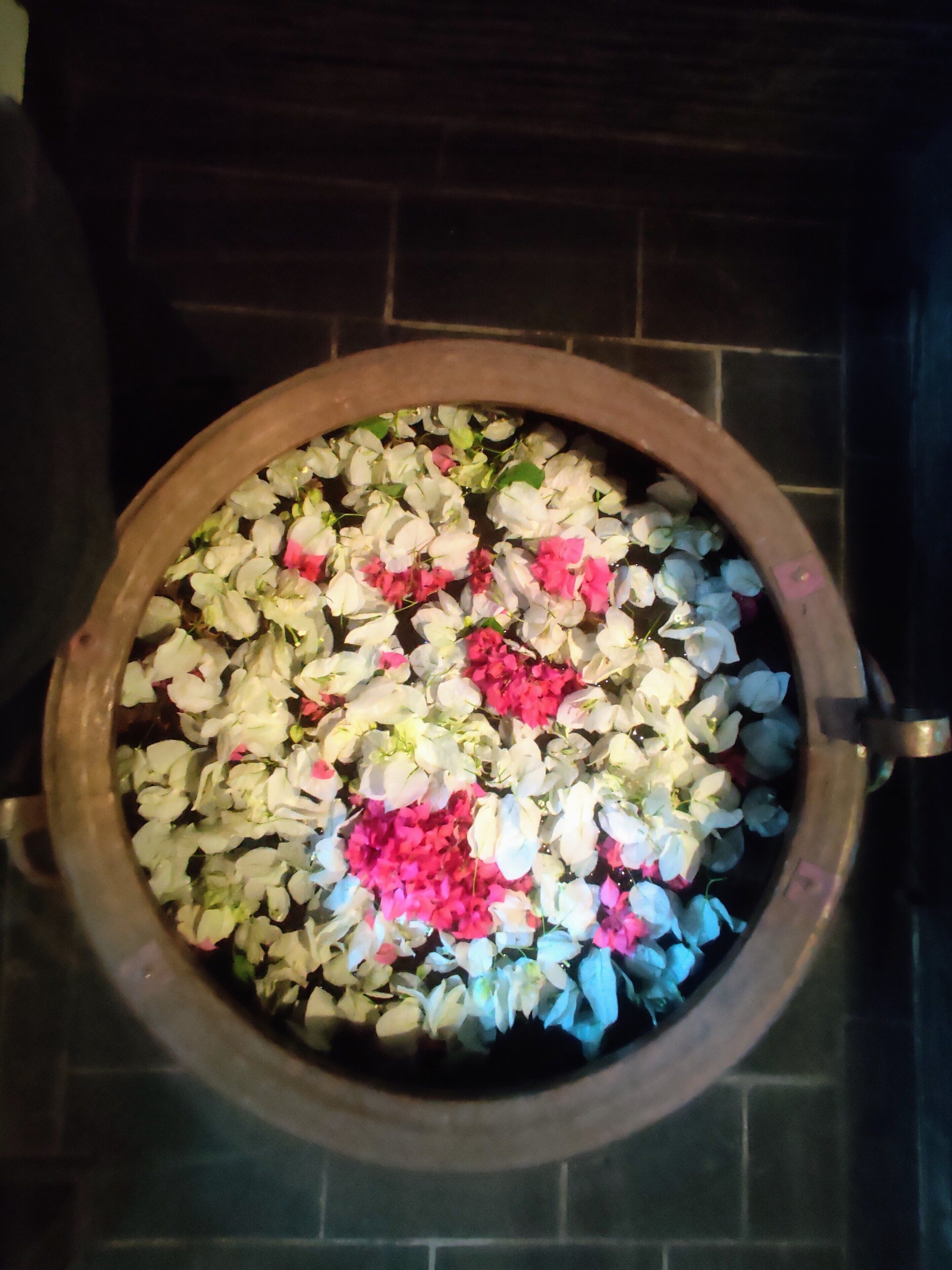 Un tazón de madera grande lleno de flores blancas y rosas, sobre un piso de baldosas.