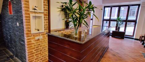 A reception area with a brick wall, a glass-top counter, and potted plants.