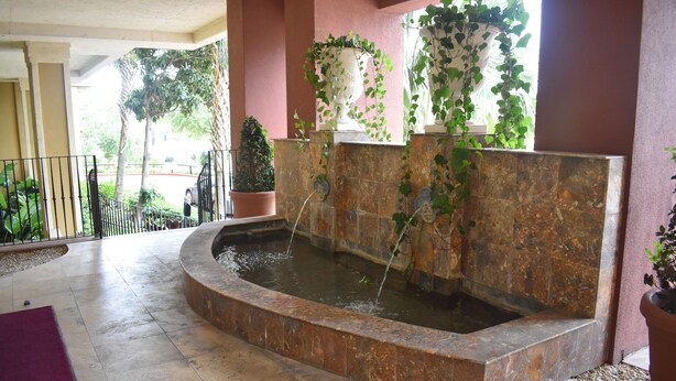 A water feature with a fountain, surrounded by potted plants and a tiled floor.
