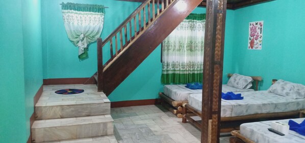 A staircase with wooden railings leading to a room with two beds, a small rug, and a wall with a poster.