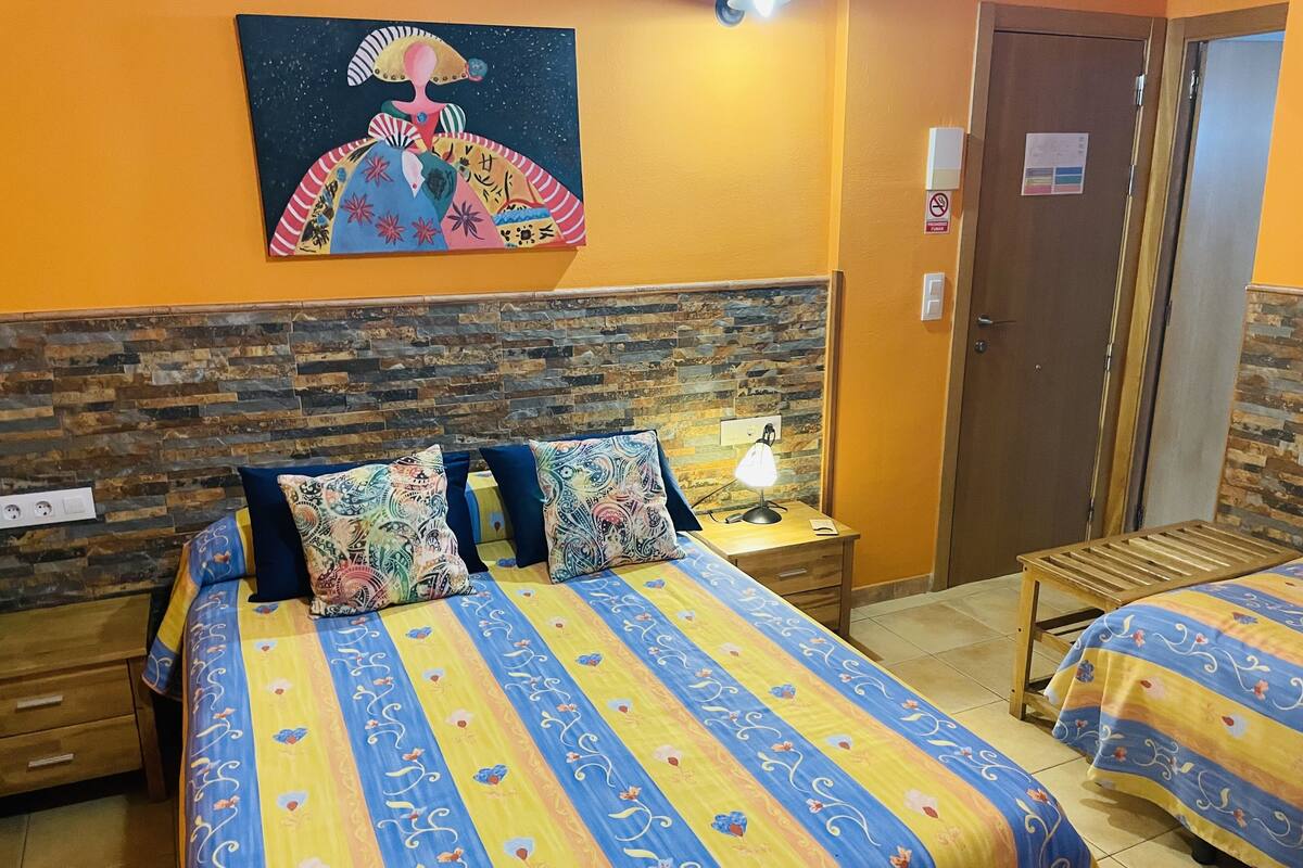 A hotel room with a bed, a nightstand, a lamp, a painting on the wall, and a door.