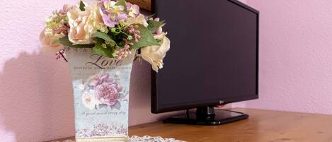 A desk with a vase of flowers, a computer monitor, and a doily.