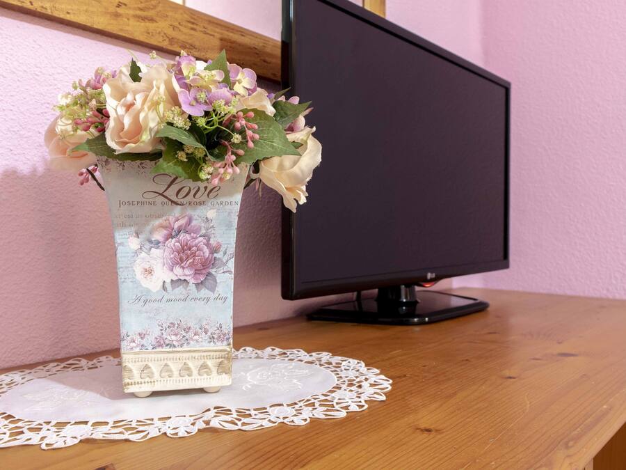 Ein Schreibtisch mit einer Blumenvase, einem Computermonitor und einer Tischdecke.