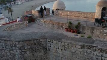 Un paisaje urbano costero con un muro de piedra destacada, una estructura en forma de cúpula y vistas a la playa y al océano.