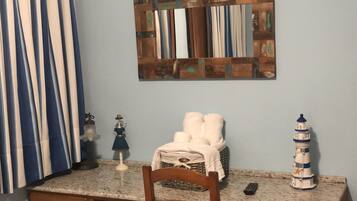 A kitchen with a wooden chair, a small table, a basket with towels, a decorative lighthouse, and a wall-mounted mirror.