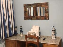 A kitchen with a wooden chair, a small table, a basket with towels, a decorative lighthouse, and a wall-mounted mirror.