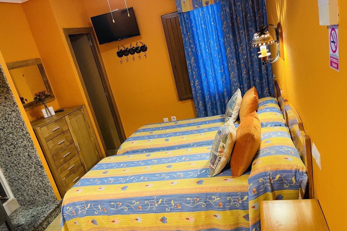 A bedroom with a bed, wooden dresser, and a TV mounted on the wall.