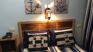 A bed with striped bedding, two pillows with nautical designs, a wall-mounted light, and two nautical-themed wall art pieces.