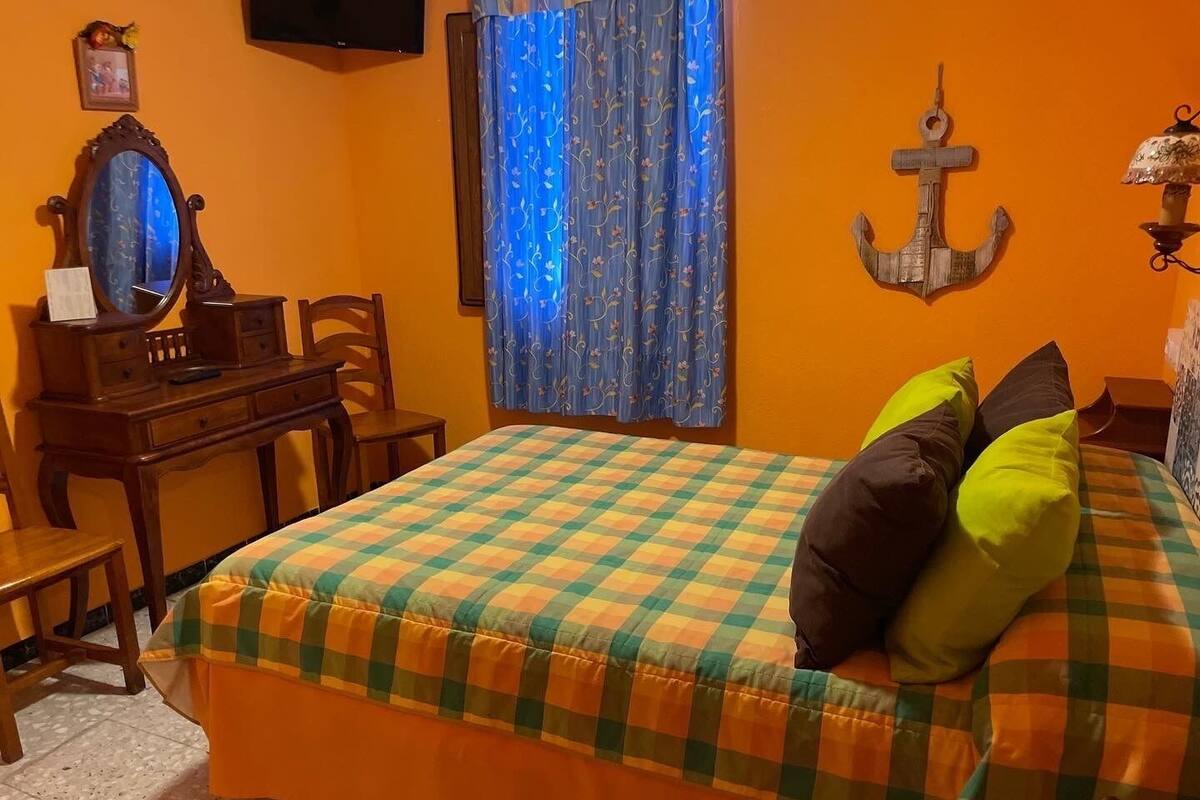 A bedroom with a bed, a desk, a chair, a mirror, and a curtain.