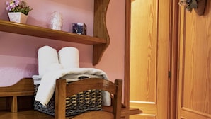 A wooden chair with a woven basket and a striped cushion, a wooden desk with a towel and a small potted plant, and a wooden door with a basket of flowers.