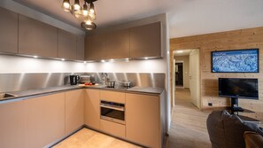 A modern kitchen with stainless steel appliances, a built-in oven, and a wooden dining area with a television. - Flat 6 pers - modern, central, ski in ski out (CHATEL)