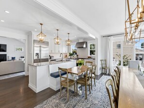 A modern kitchen with a central island, pendant lighting, and a dining area with a long table and chairs.
