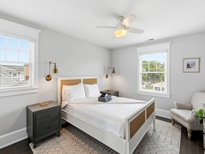 A bedroom with a bed, nightstand, chair, and a ceiling fan.
