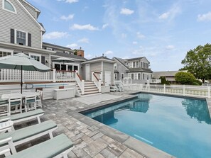 Une piscine résidentielle entourée d’une clôture blanche, avec des marches menant à une terrasse et du mobilier d’extérieur.