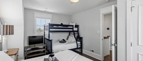 Een slaapkamer met een stapelbed, een televisie, een bureau en een deur naar een andere kamer.