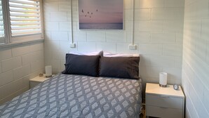 Un dormitorio con una cama, dos mesitas de noche, un velador, un cuadro colgado en la pared y una ventana con persianas.