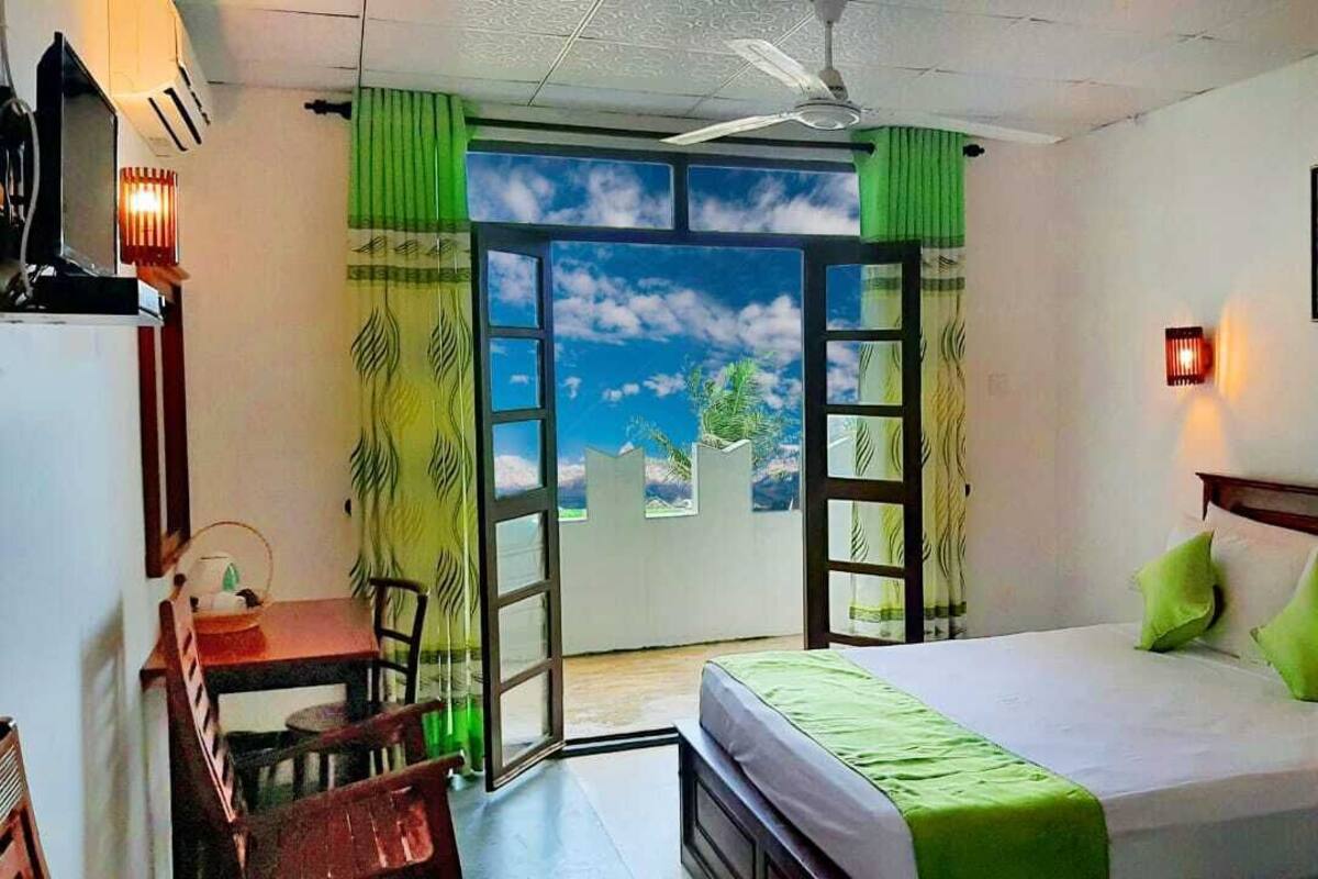 A hotel room with a bed, a desk, and a chair. There is a window with a view of the sky and clouds.
