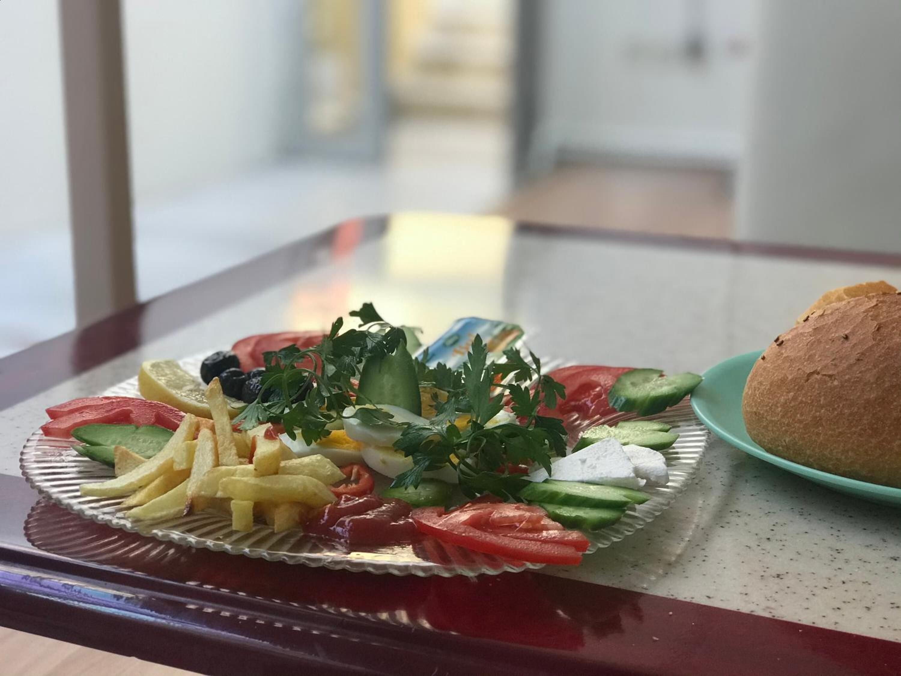 A plate of food with vegetables, cheese, and bread on a glass table.