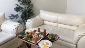 A dining table with a variety of dishes, including eggs, salads, and bread, set on a beige leather couch in a room with a large plant. - Kalkedon Hostel (Istanbul)