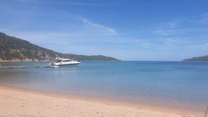 A boat docked at a sandy beach with calm water and hills in the background. - Villa Bonifacio 12p, swimming pool -1km from the port Preserved and exceptional environment (Bonifacio)