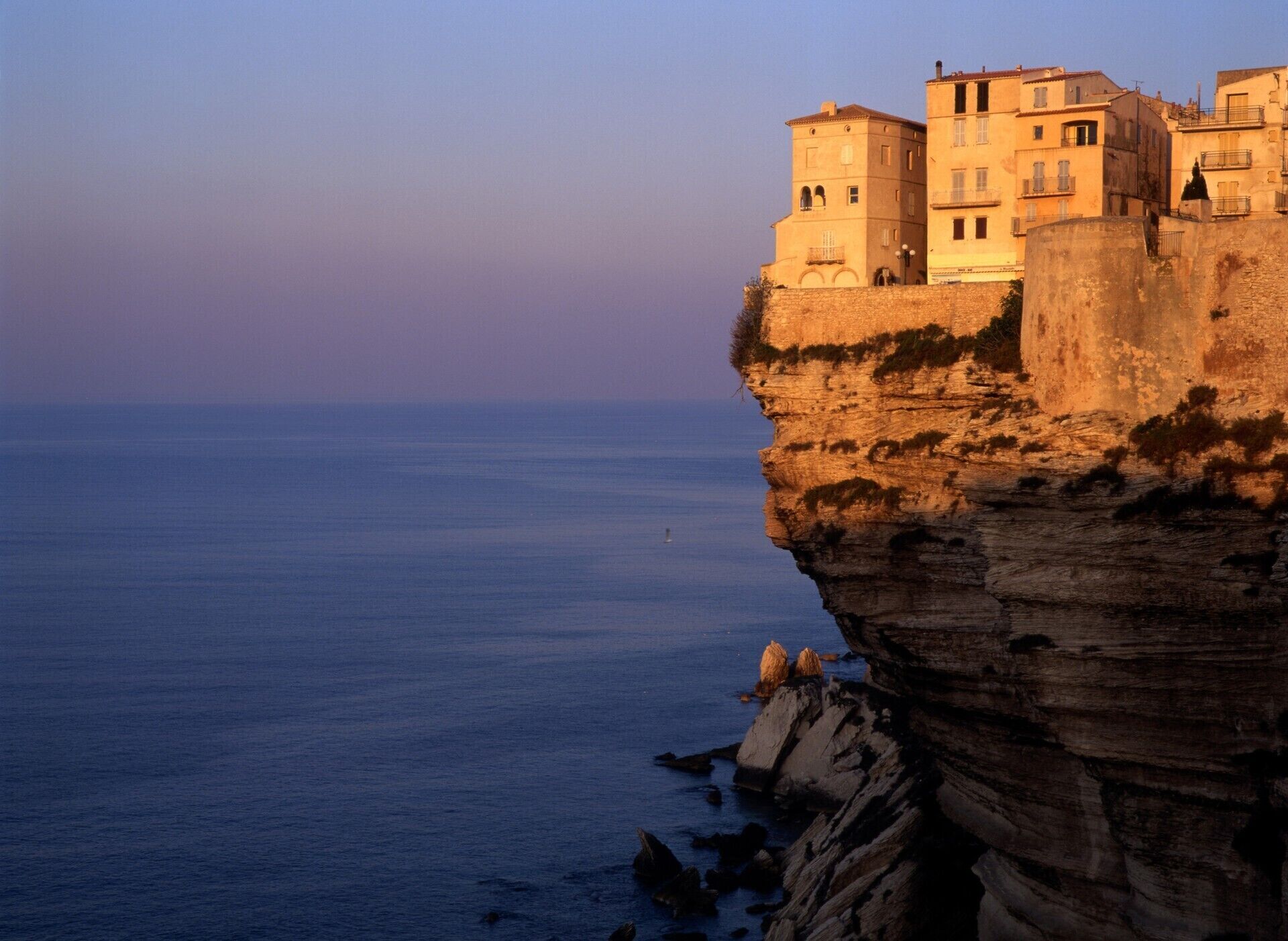 A coastal cliff with buildings perched on top, overlooking the sea.