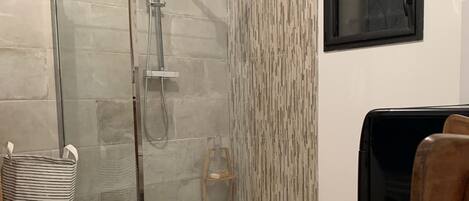 Un baño con cabina de ducha de vidrio, una silla de madera, una cesta de mimbre y un papel tapiz estampado.
