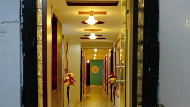 A hotel corridor with a wooden floor, decorative ceiling lights, and floral arrangements. - Hotel Royal Stay (Ahmedabad)