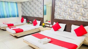 A hotel room with three single beds, each with white bedding and red accents, a wooden headboard, and a geometric-patterned wall. - Hotel Royal Stay (Ahmedabad)