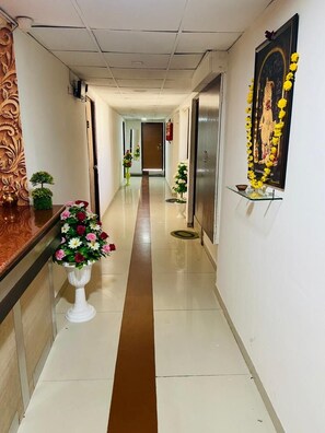 A hotel corridor with a reception desk, a white vase with flowers, a framed picture, and a brown stripe on the floor. - Hotel Royal Stay (Ahmedabad)
