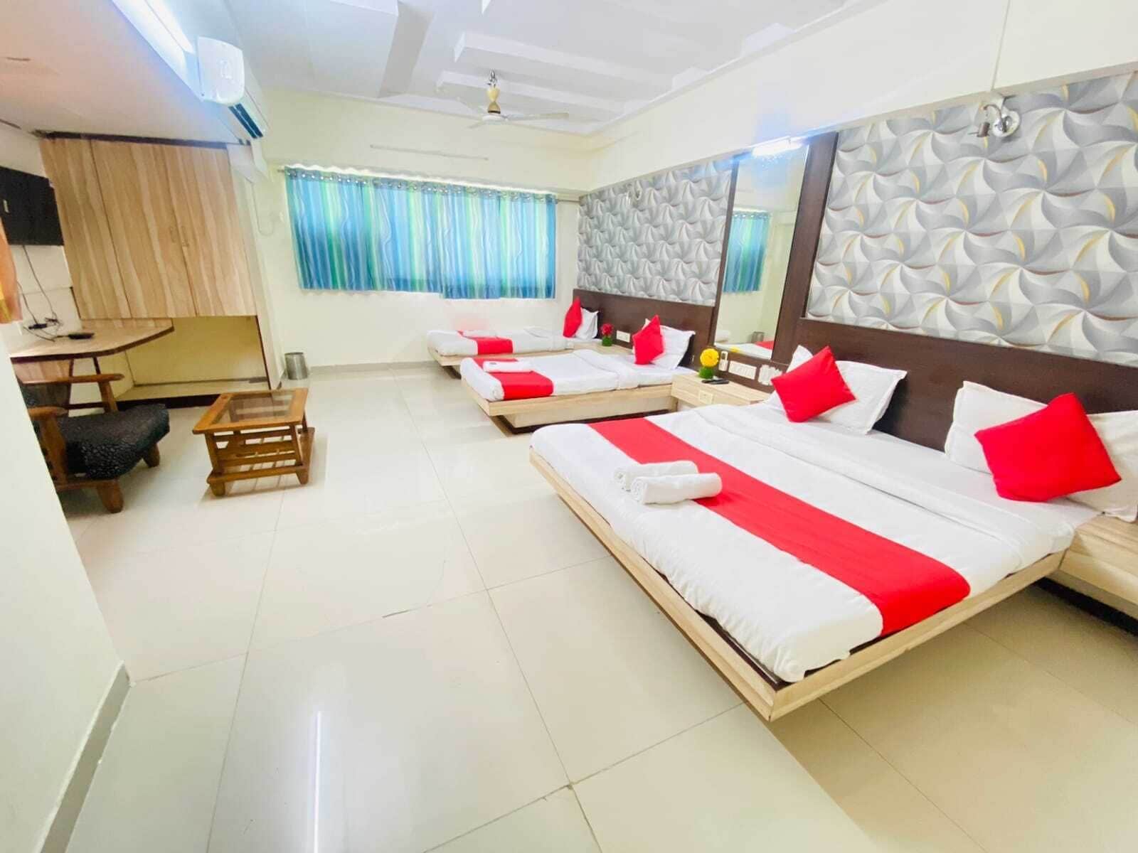 Habitación de hotel con tres camas, un escritorio de madera, una silla y una mesita.