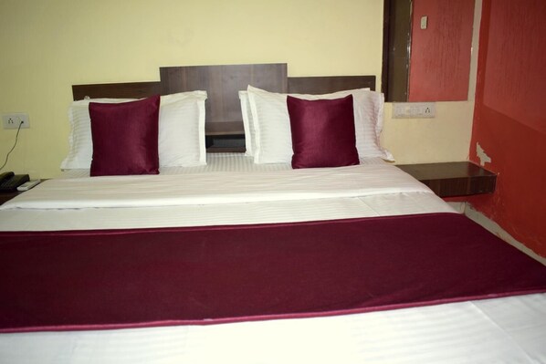 A neatly made bed with white linens and two dark red pillows, a wooden headboard, and a red wall. - Hotel Royal Stay (Ahmedabad)