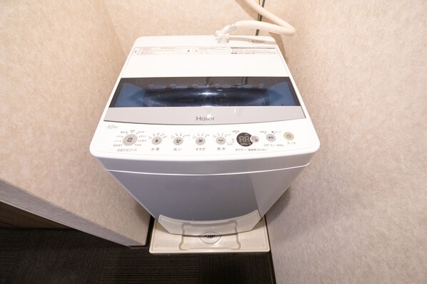 A white Haier washing machine with a control panel, a water inlet hose, and a drain hose. - Bright Hotel Kiyomizu (Kyoto)