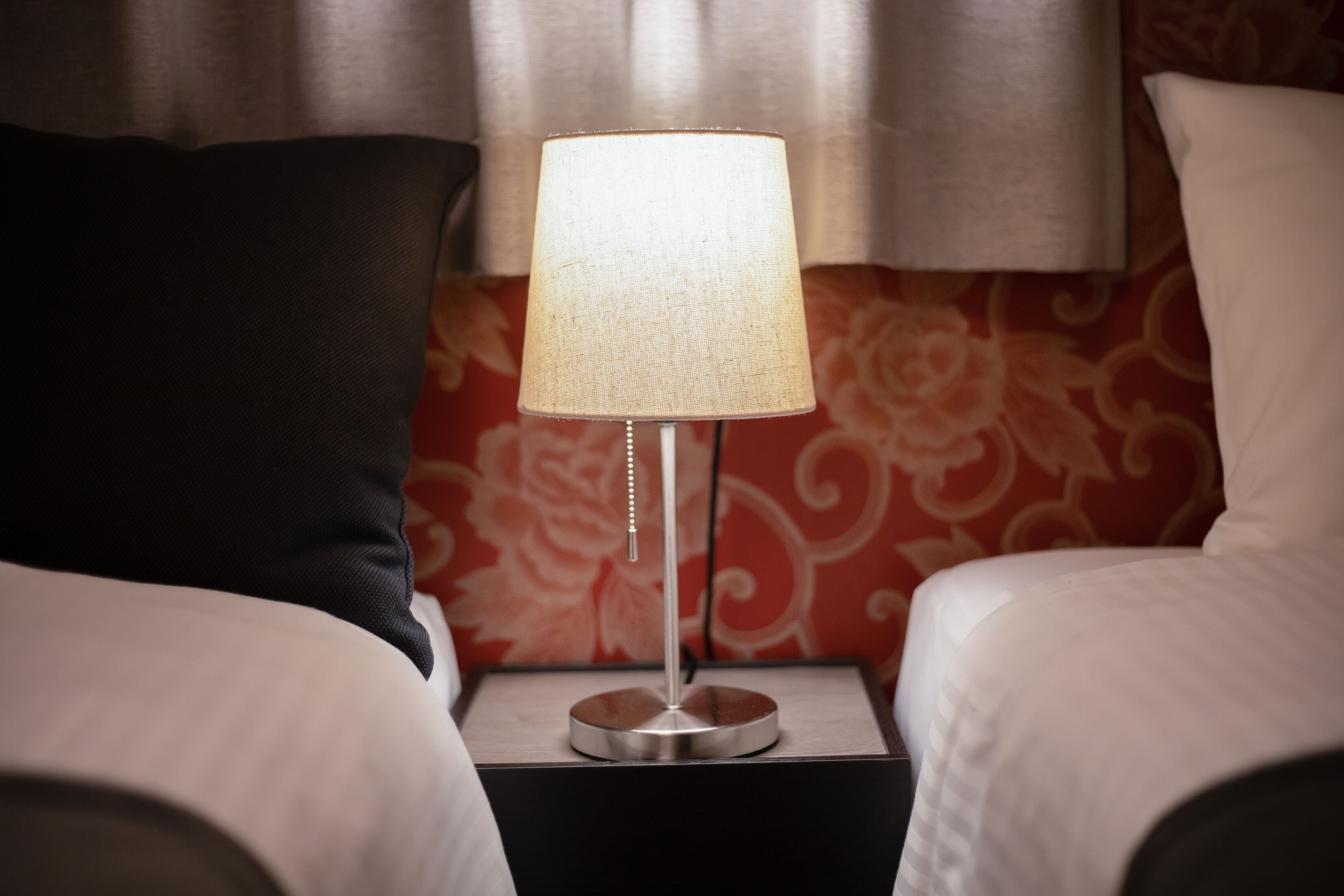 A bed with white bedding, a black pillow, and a bedside table with a lamp.