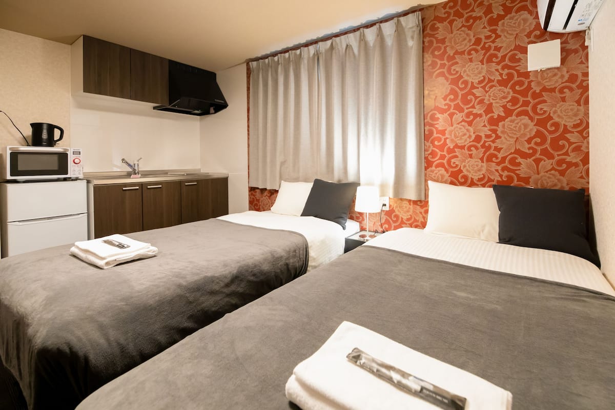 Quarto de hotel com duas camas, cozinha compacta e banheiro.