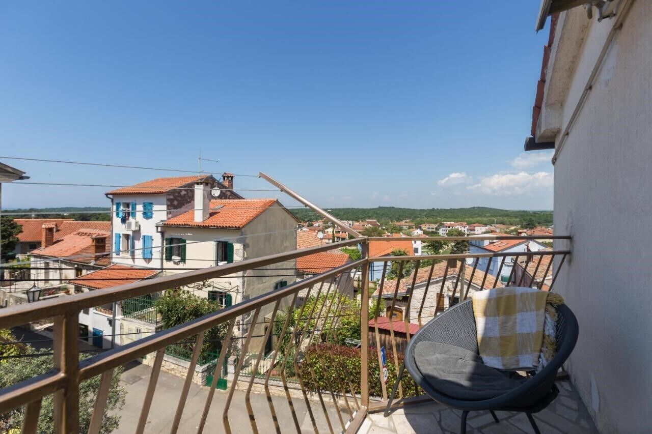Ein Balkon mit Stuhl, Geländer und Blick auf Gebäude und Grünflächen.