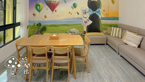 A cozy room with a wooden dining table and chairs, a beige sofa, and a mural of hot air balloons on the wall. - Youge Homestay (Taitung)