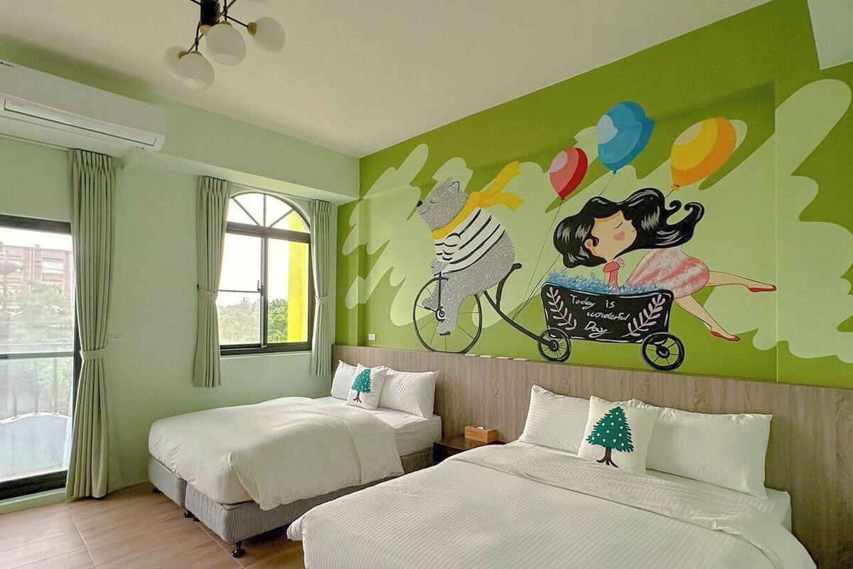 A hotel room with two beds, a mural on the wall, and a large window.