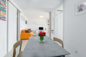Un salon moderne avec une table à manger grise, un canapé orange et un téléviseur en arrière-plan.