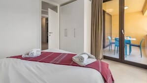 A hotel room with a bed, a red and white bedspread, a white towel, a sliding glass door to a balcony, and a dining area visible through the door. - Right in the Porec center, near the beach,WiFi,air conditioning,garage, elevator (Porec)